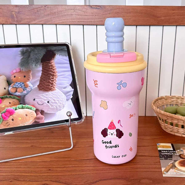 Pink children's cup with cartoon designs on a wooden table next to a tablet displaying cartoon characters.
