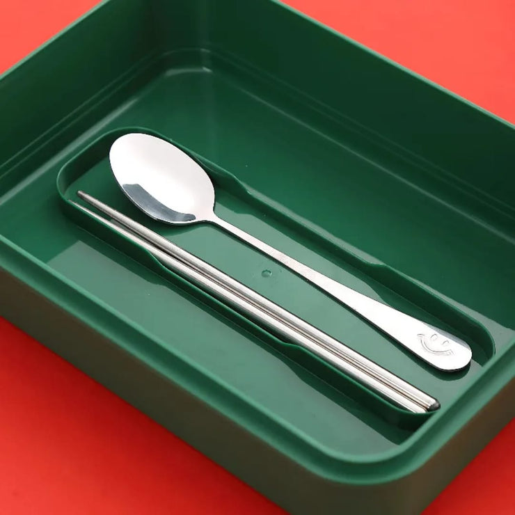 Silver spoon and chopsticks in a green tray on a red background
