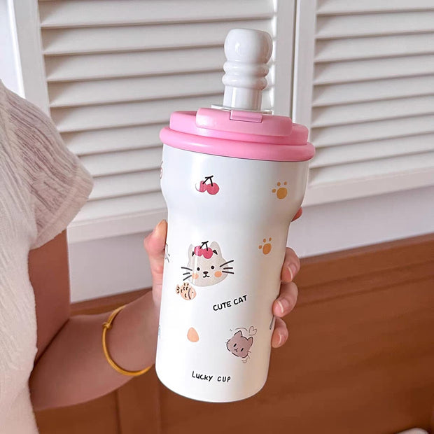 Person holding a white cup with pink lid featuring cartoon cat designs.