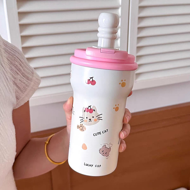 Person holding a white cup with pink lid featuring cartoon cat designs.